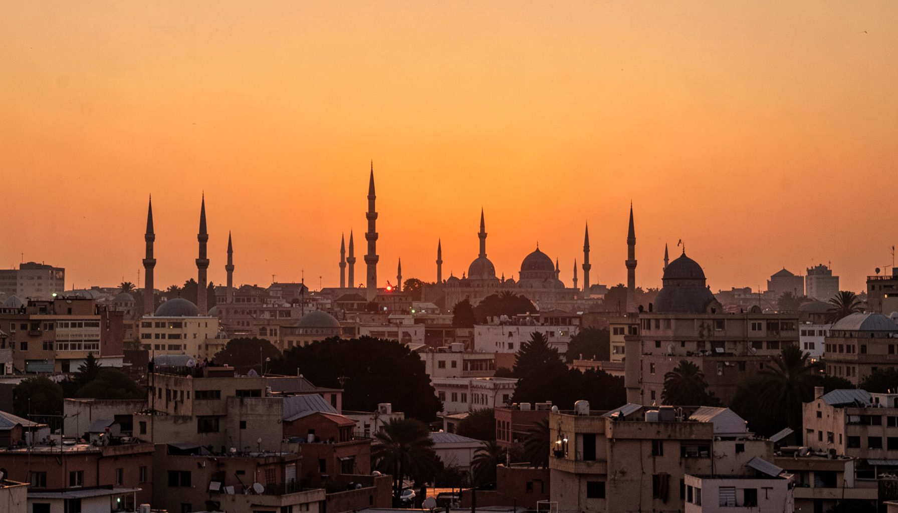 Cairo's cityscape with minarets silhouetted against a warm desert sunset, rich amber and terracotta hues